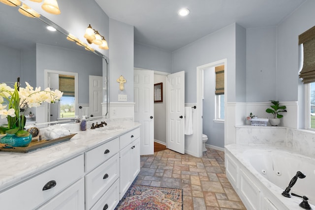 bathroom featuring toilet, a wealth of natural light, a tub with jets, stone finish floor, and vanity