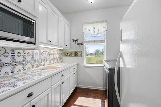 kitchen with freestanding refrigerator, a sink, light countertops, stainless steel microwave, and backsplash