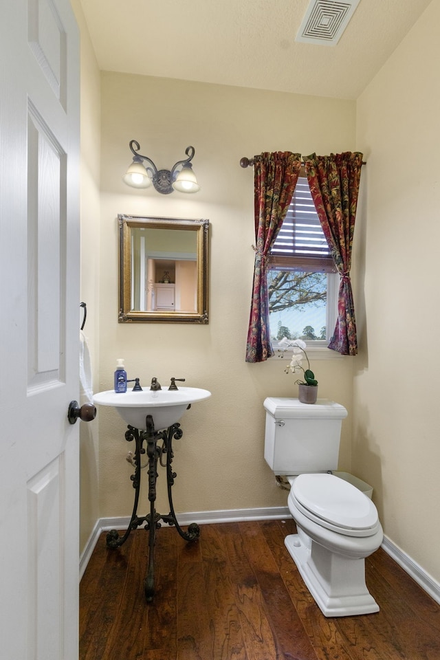 half bath with visible vents, baseboards, toilet, and wood finished floors