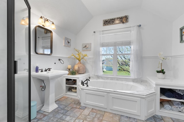 bathroom with lofted ceiling, stone finish flooring, a bath, and wainscoting