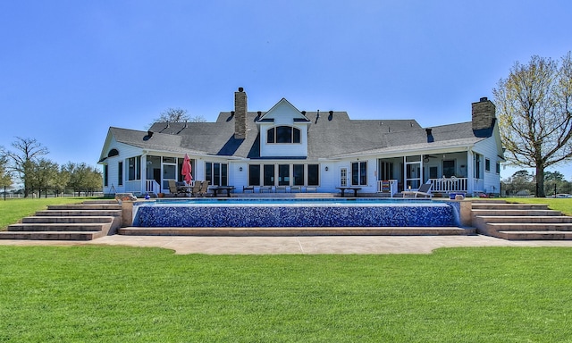 rear view of house with an outdoor pool, a yard, a chimney, and a sunroom