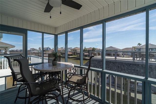 sunroom with lofted ceiling, a ceiling fan, a residential view, and a water view