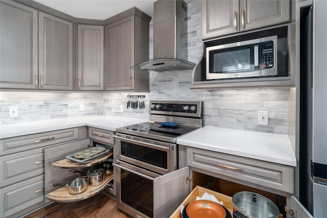 kitchen featuring decorative backsplash, gray cabinetry, wall chimney exhaust hood, and stainless steel appliances