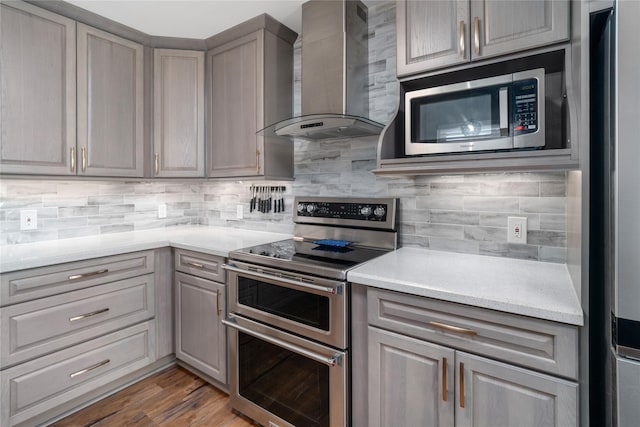 kitchen with stainless steel appliances, backsplash, gray cabinetry, and wall chimney exhaust hood