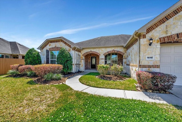 view of front of home with a front yard, fence, roof with shingles, an attached garage, and stone siding