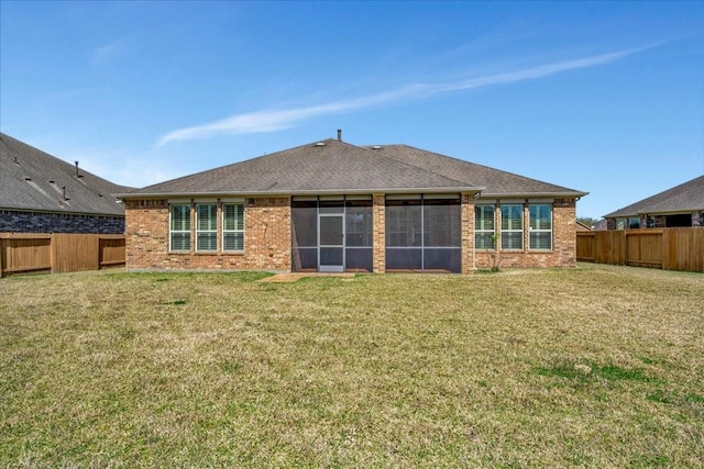 rear view of house with a yard, brick siding, a fenced backyard, and a sunroom