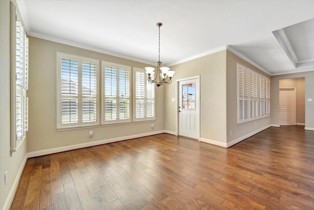 empty room with a chandelier, ornamental molding, baseboards, and wood finished floors