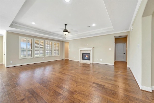 unfurnished living room with a raised ceiling, wood finished floors, a high end fireplace, and ceiling fan