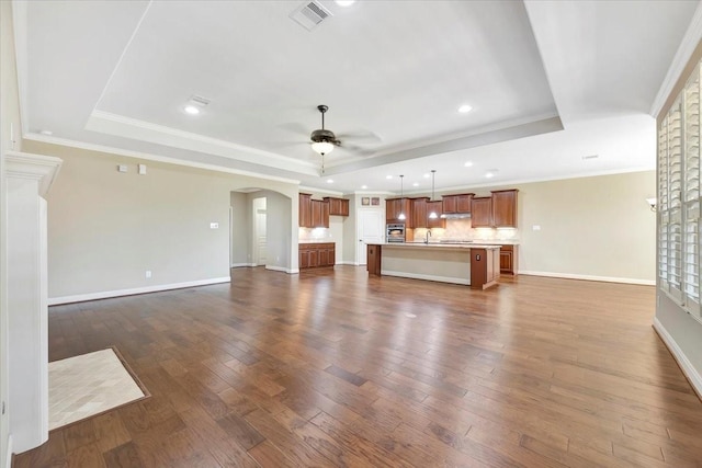 unfurnished living room with a ceiling fan, dark wood-style floors, visible vents, arched walkways, and a raised ceiling