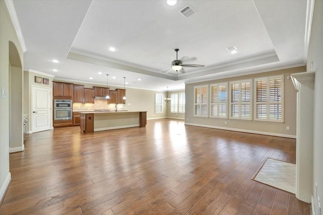 unfurnished living room featuring a tray ceiling, visible vents, dark wood-style floors, and a ceiling fan