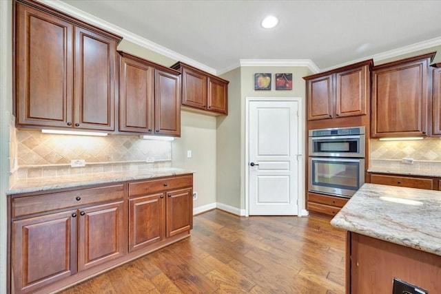 kitchen featuring light stone counters, wood finished floors, stainless steel double oven, and ornamental molding