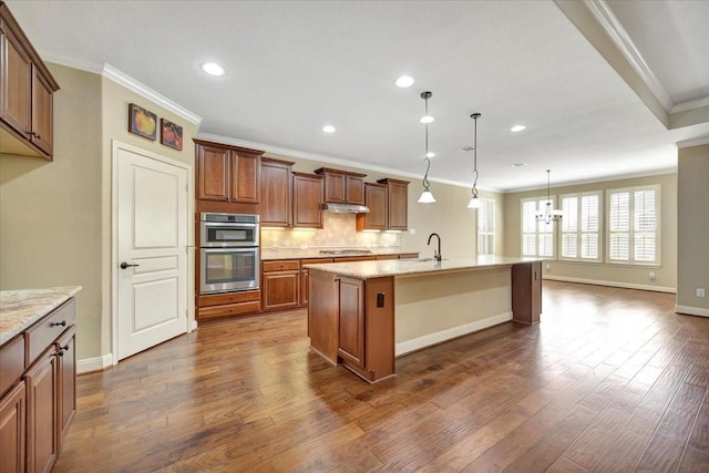 kitchen with dark wood-type flooring, an island with sink, crown molding, and under cabinet range hood