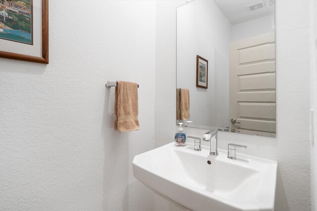 bathroom featuring visible vents, a textured wall, and a sink