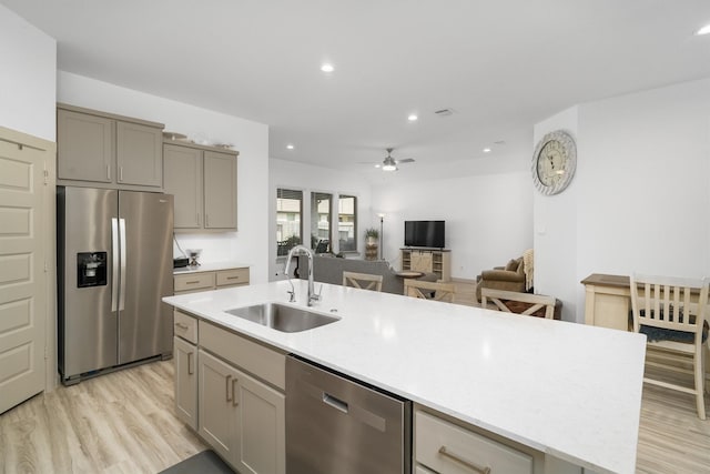 kitchen with an island with sink, gray cabinets, a sink, light wood-style floors, and appliances with stainless steel finishes