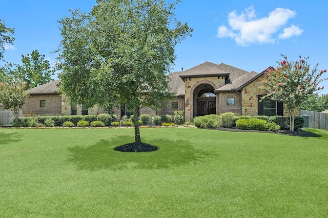 view of front facade with stone siding, a shingled roof, a front lawn, and fence