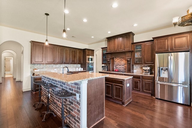 kitchen featuring a center island with sink, arched walkways, and appliances with stainless steel finishes