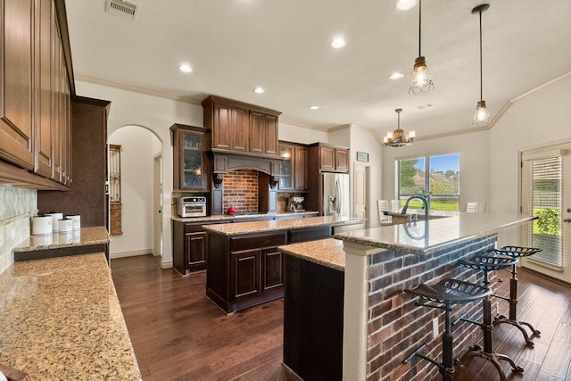 kitchen featuring visible vents, an island with sink, stainless steel refrigerator with ice dispenser, dark wood finished floors, and arched walkways