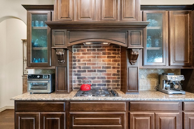 kitchen featuring light stone counters, decorative backsplash, glass insert cabinets, and stainless steel gas stovetop