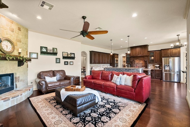 living area featuring arched walkways, visible vents, ceiling fan with notable chandelier, and a fireplace