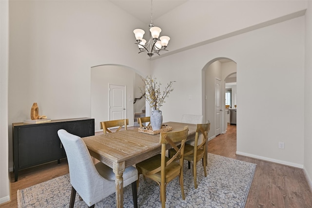 dining area featuring wood finished floors, baseboards, high vaulted ceiling, arched walkways, and a notable chandelier