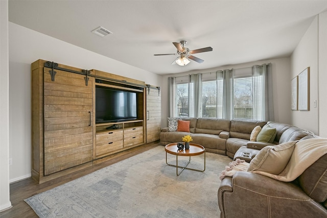 living area with visible vents, ceiling fan, baseboards, a barn door, and wood finished floors