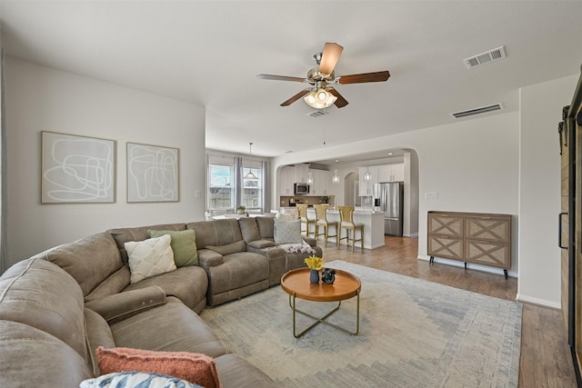 living room with ceiling fan, arched walkways, visible vents, and light wood-type flooring