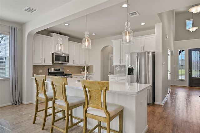 kitchen with visible vents, light wood-type flooring, appliances with stainless steel finishes, arched walkways, and white cabinets