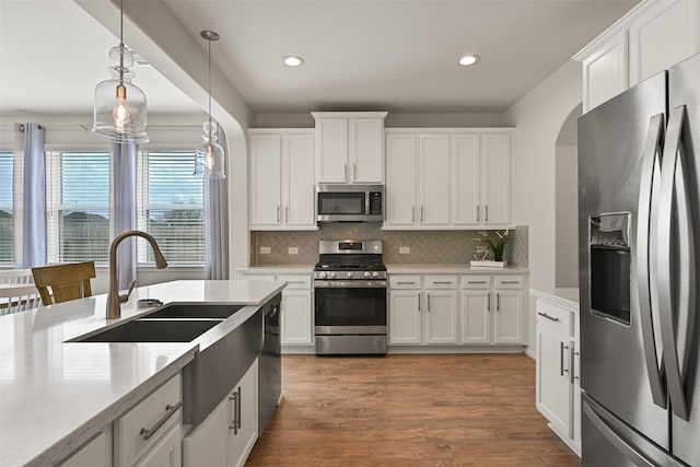 kitchen featuring pendant lighting, wood finished floors, white cabinetry, appliances with stainless steel finishes, and decorative backsplash