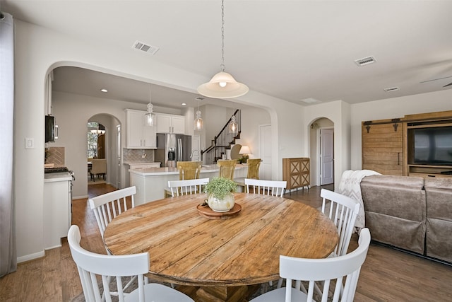 dining space featuring visible vents, arched walkways, wood finished floors, and stairs