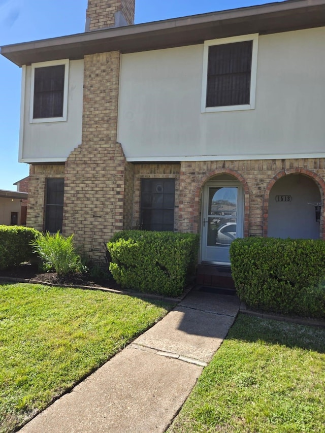 view of front of home with brick siding, stucco siding, a chimney, and a front lawn