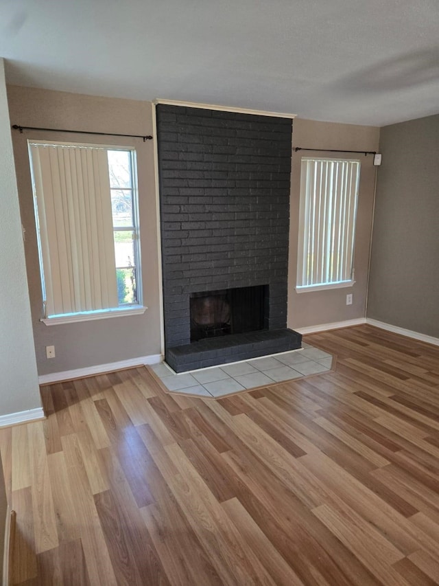 unfurnished living room featuring a fireplace, baseboards, and wood finished floors