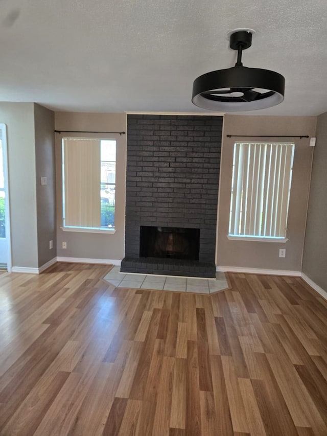 unfurnished living room featuring wood finished floors, a fireplace, baseboards, and a textured ceiling