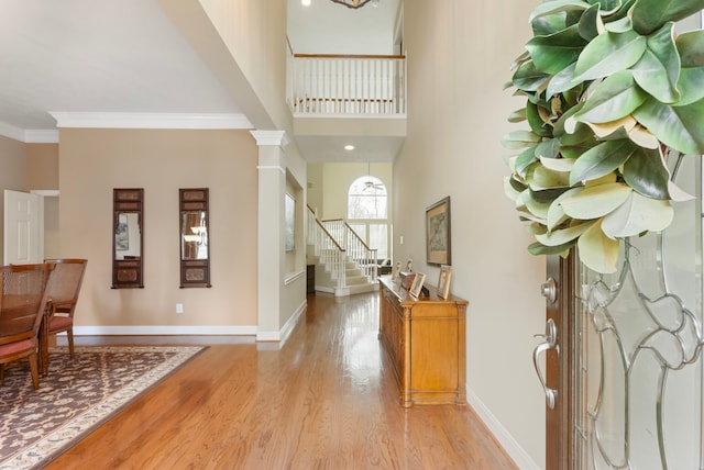 entryway with light wood-type flooring, crown molding, decorative columns, baseboards, and stairs