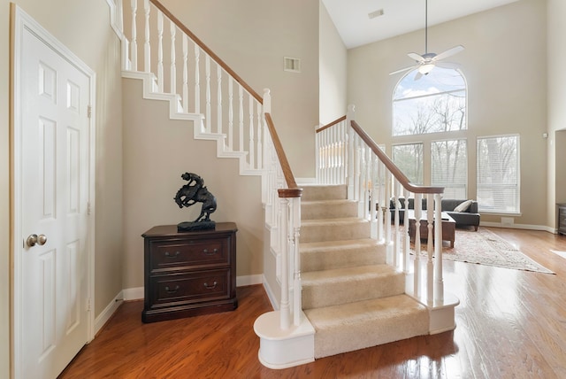 stairs with visible vents, baseboards, a towering ceiling, and wood finished floors