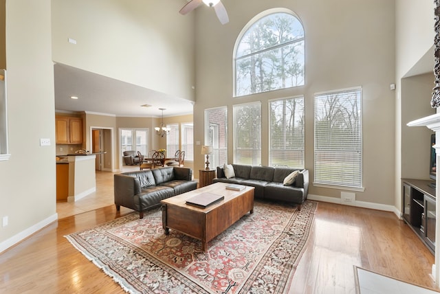 living room with ceiling fan with notable chandelier, crown molding, baseboards, and light wood-type flooring