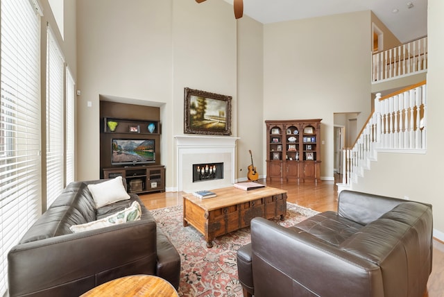 living area featuring wood finished floors, baseboards, stairs, a towering ceiling, and a glass covered fireplace