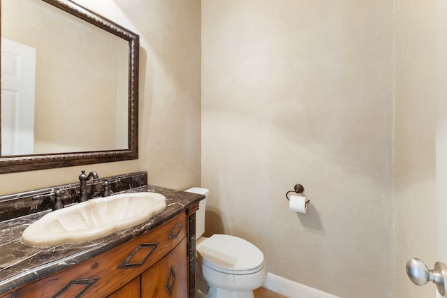 half bath featuring baseboards, toilet, and vanity