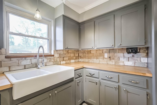 kitchen featuring decorative backsplash, butcher block countertops, gray cabinets, and a sink