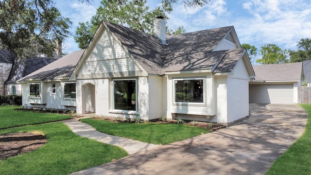 english style home featuring a shingled roof, a front yard, brick siding, and a chimney