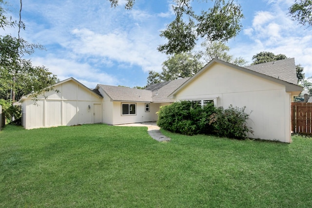 rear view of house with stucco siding, roof with shingles, a yard, and fence