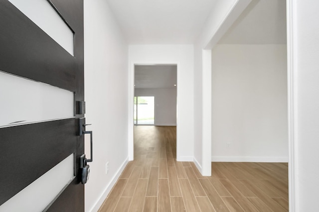 corridor with light wood-type flooring and baseboards