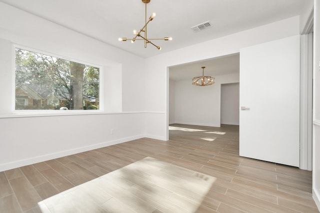 spare room featuring a notable chandelier, baseboards, visible vents, and wood finish floors