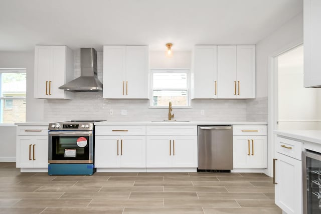 kitchen featuring a sink, stainless steel appliances, wine cooler, wall chimney exhaust hood, and white cabinets