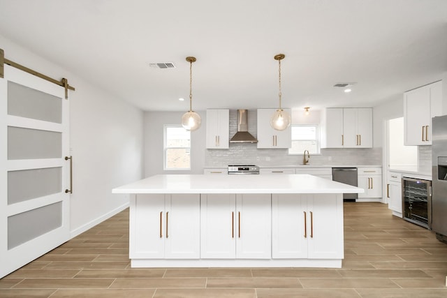 kitchen with visible vents, wall chimney range hood, beverage cooler, a barn door, and appliances with stainless steel finishes