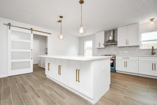 kitchen with visible vents, a barn door, stainless steel range with electric cooktop, wall chimney exhaust hood, and a sink