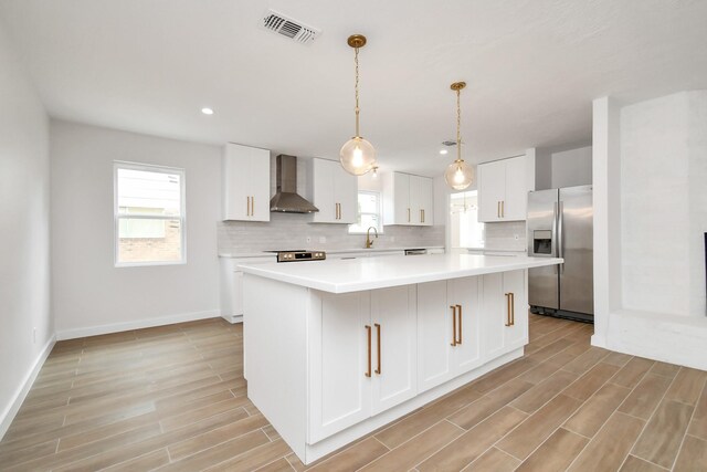 kitchen with visible vents, backsplash, appliances with stainless steel finishes, and wall chimney range hood