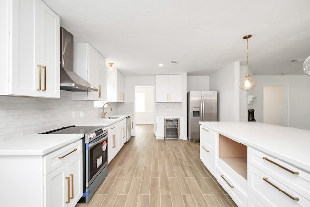 kitchen featuring wall chimney range hood, wine cooler, white cabinets, stainless steel appliances, and a sink