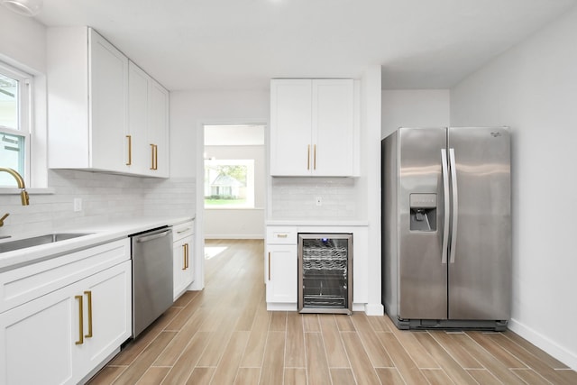 kitchen with wood finish floors, beverage cooler, a sink, stainless steel appliances, and white cabinets