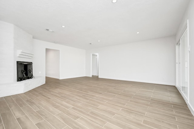 unfurnished living room with light wood-type flooring, visible vents, recessed lighting, baseboards, and a brick fireplace