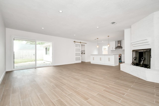 unfurnished living room with a barn door, a healthy amount of sunlight, light wood-style flooring, and visible vents